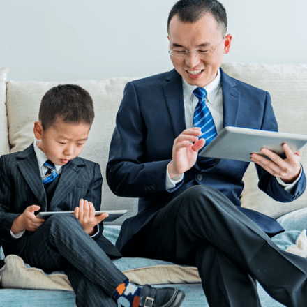 boy in business suit sitting next to man in business suit, both on their own ipad